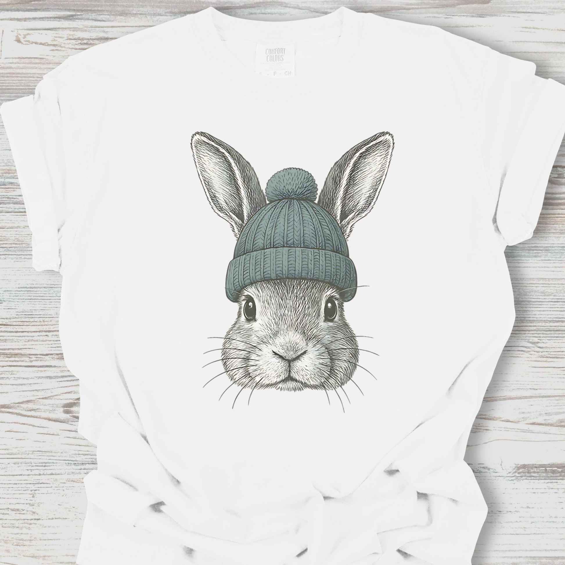 White t-shirt with a graphic of a rabbit wearing a green beanie on a wooden surface