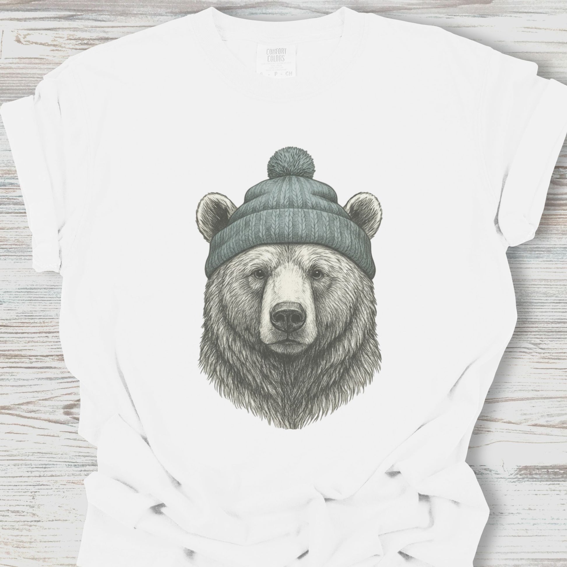 White t-shirt with a bear wearing a beanie graphic on a wooden surface