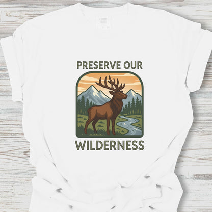 White t-shirt with a graphic of a deer and mountains, and the text 'Preserve Our Wilderness' on a wooden surface.