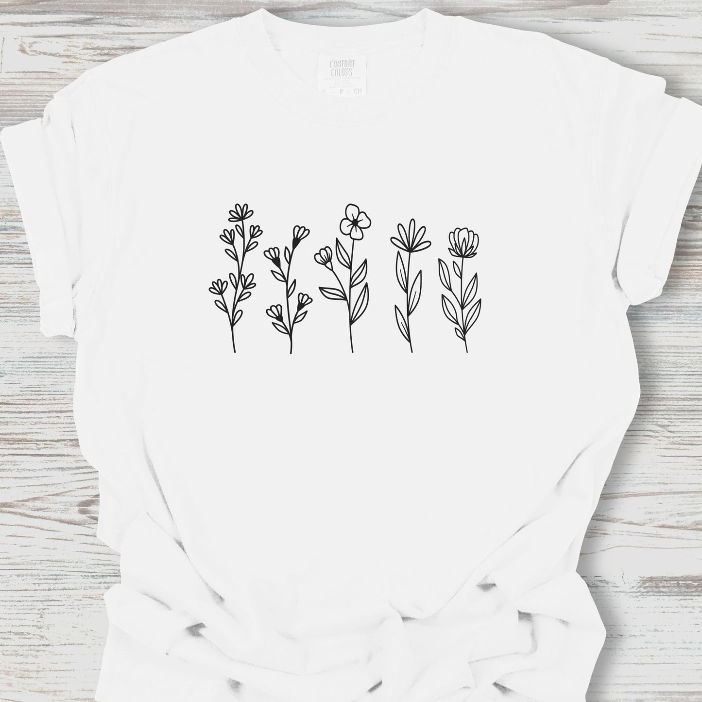 White t-shirt with black floral designs on a wooden surface