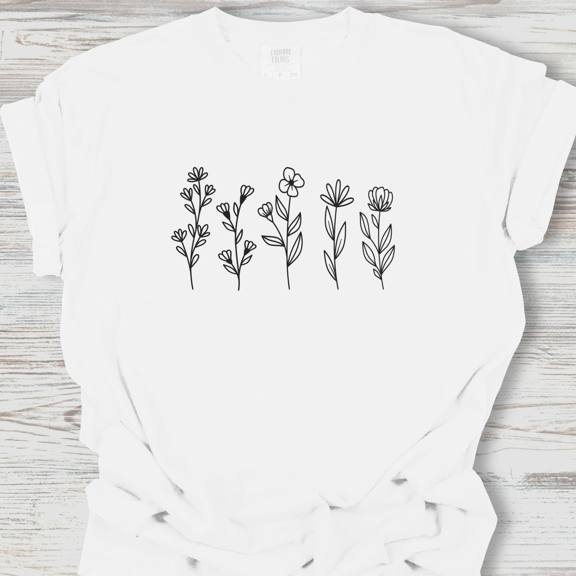 White t-shirt with black floral designs on a wooden surface