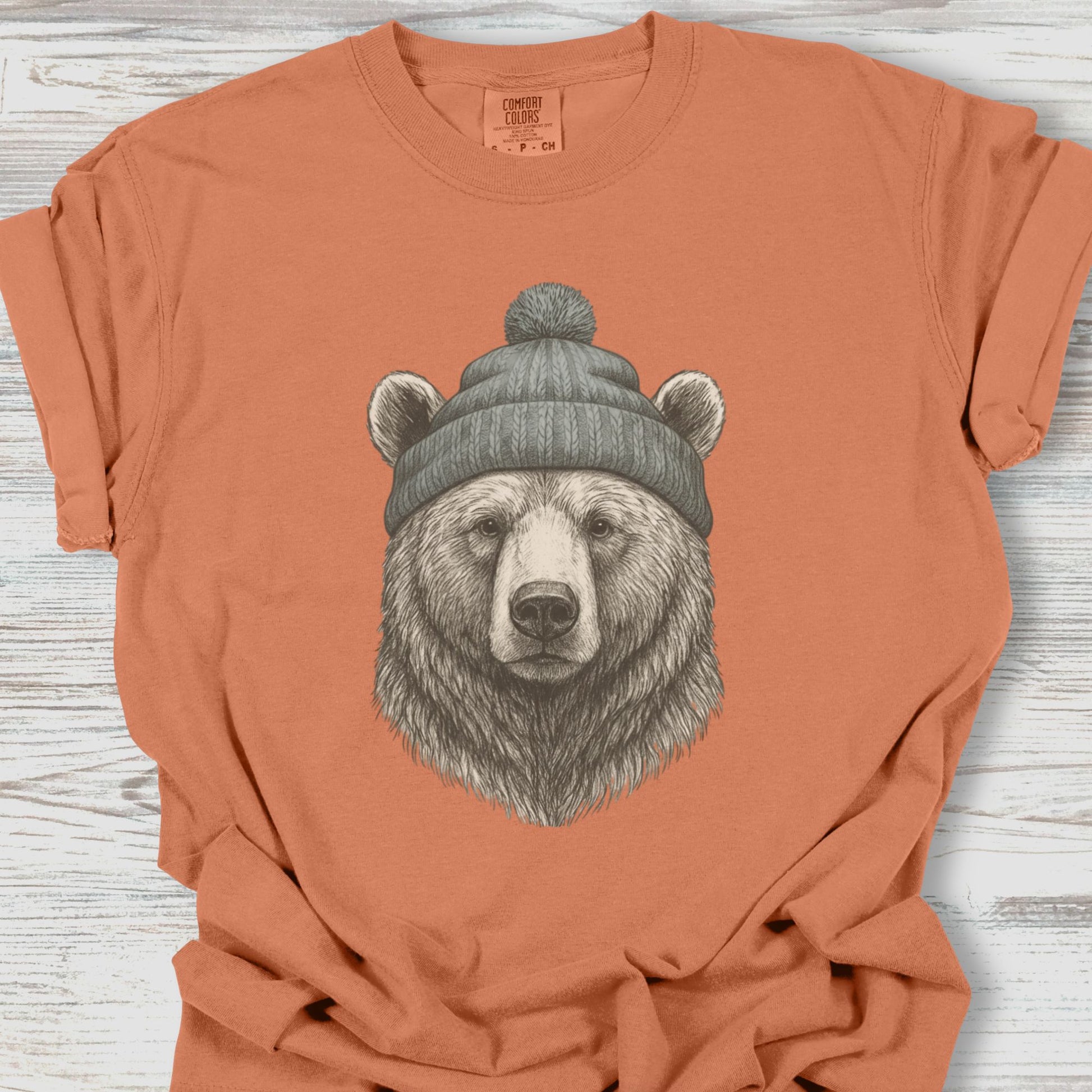Orange t-shirt with a bear wearing a hat graphic on a wooden surface