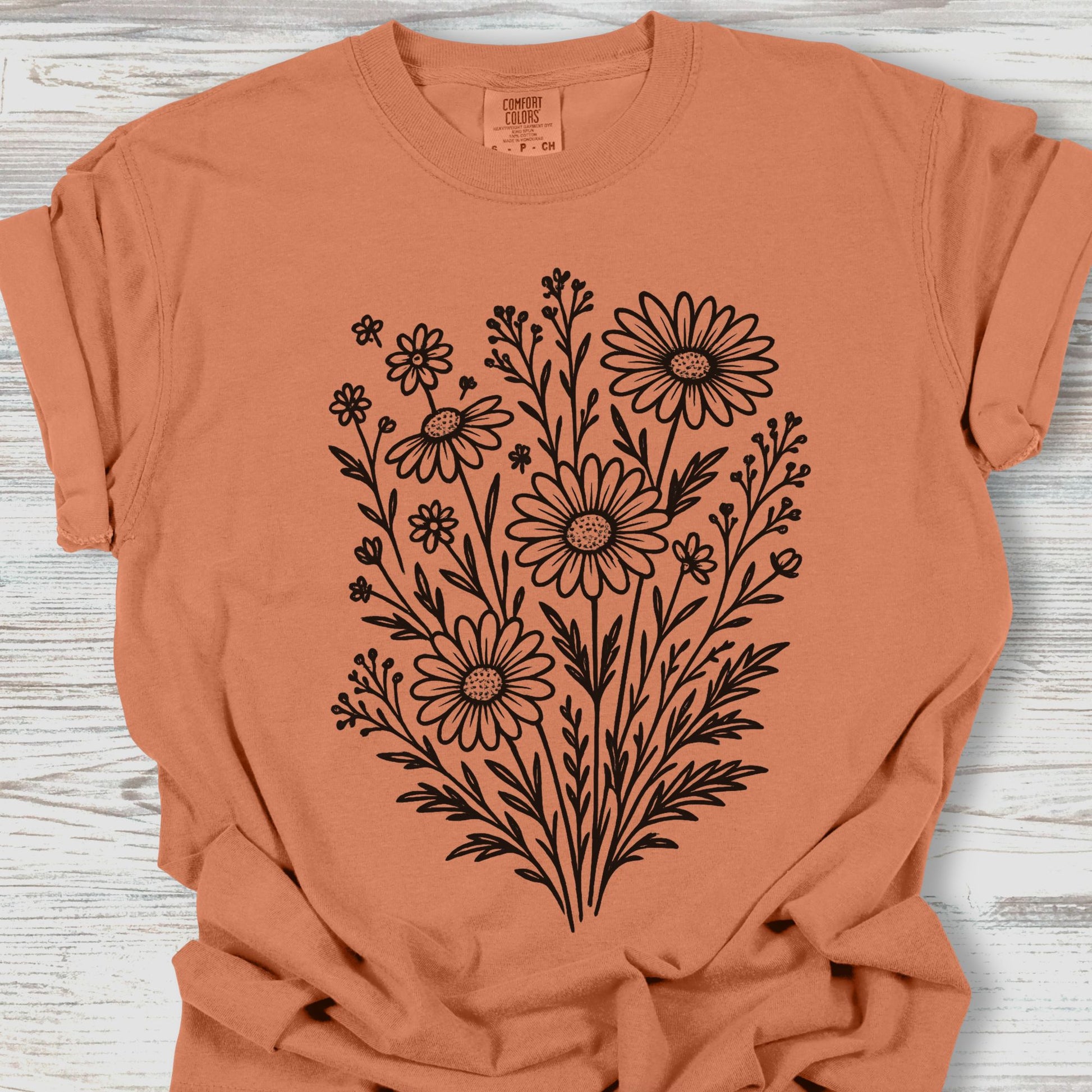 Coral t-shirt with black floral design on a wooden surface