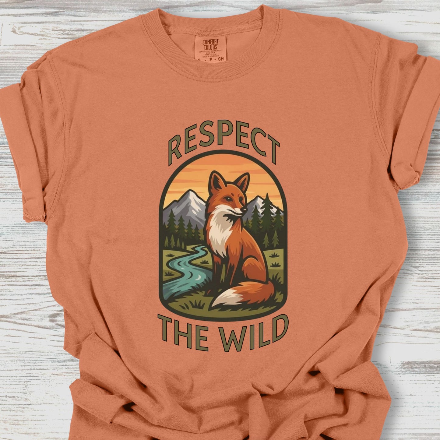 Orange t-shirt with a fox graphic and 'Respect the Wild' text on a wooden surface