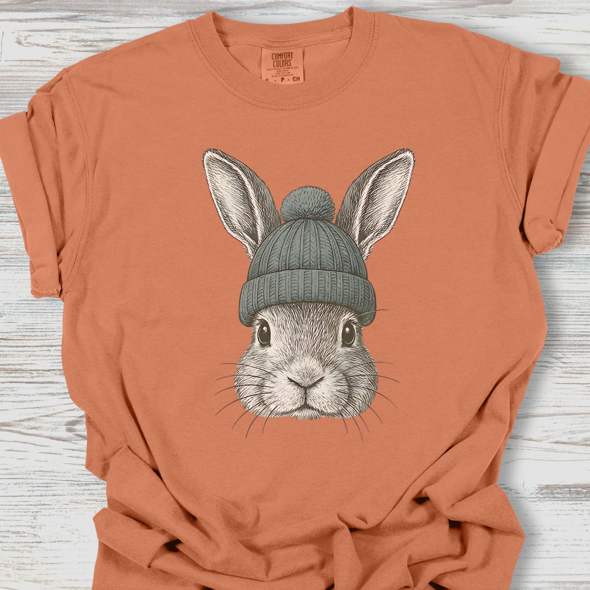 Orange t-shirt with a rabbit wearing a green beanie on a wooden surface