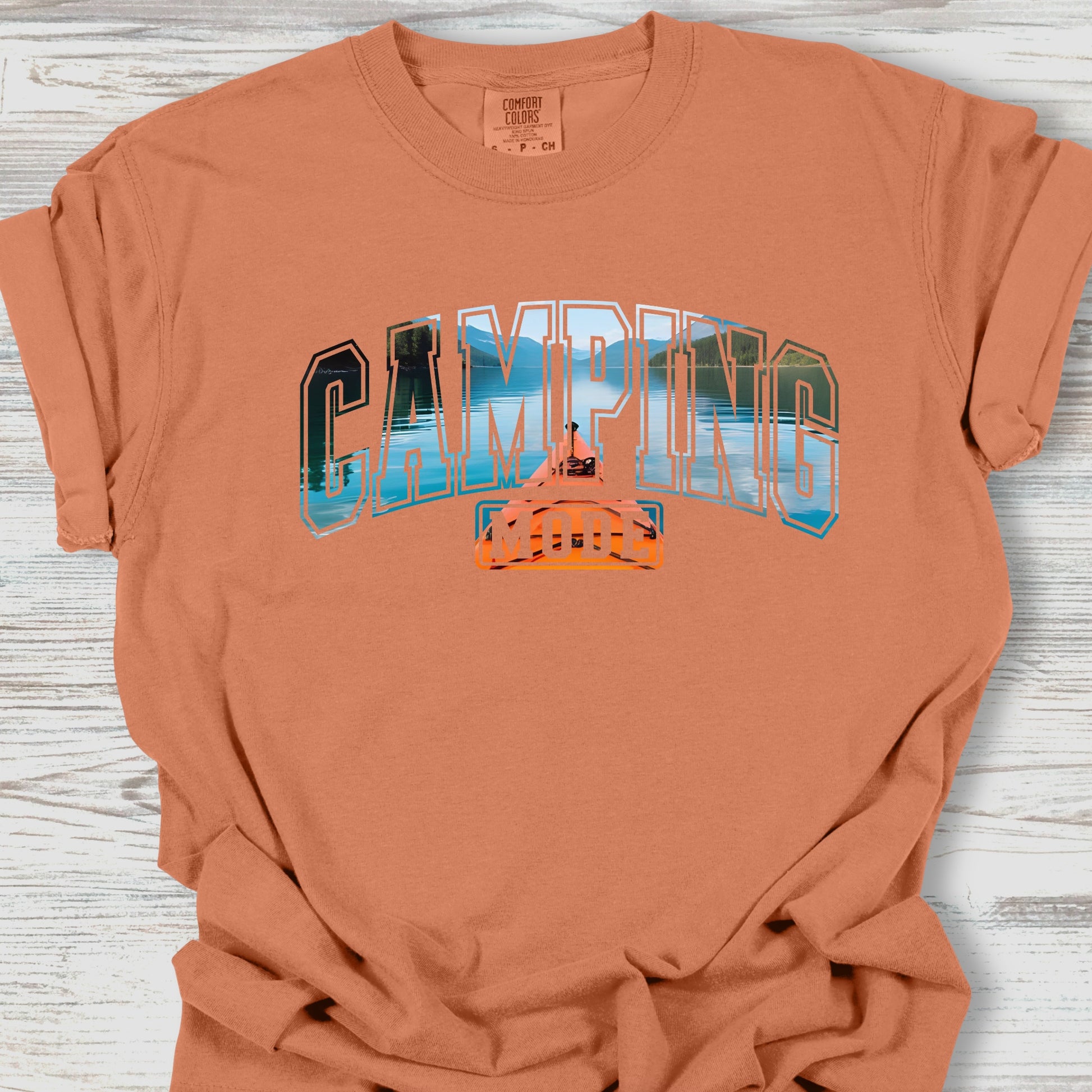 Camping-themed t-shirt with graphic design on a wooden surface