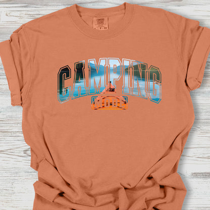 Camping-themed t-shirt with graphic design on a wooden surface