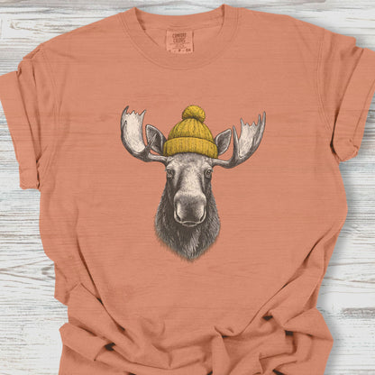 Coral t-shirt with a moose wearing a yellow beanie on a wooden surface