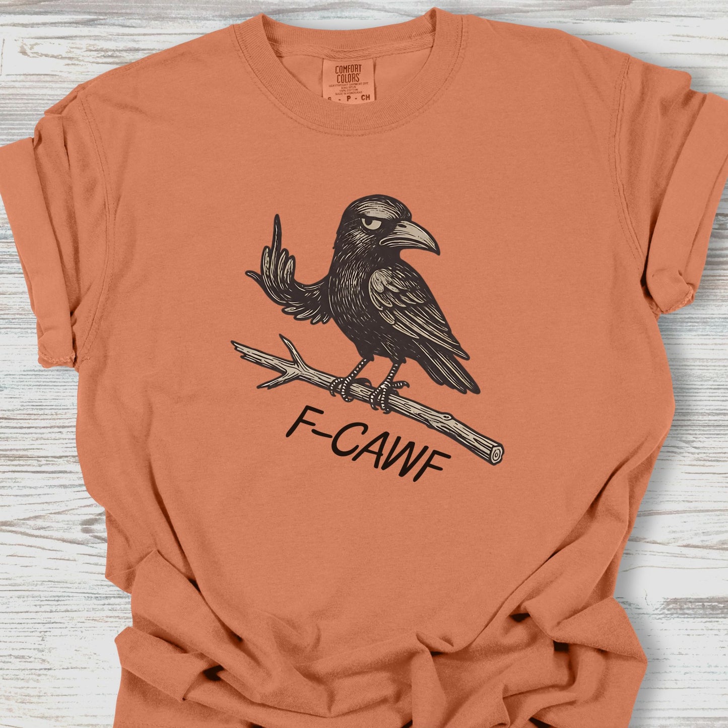 Orange t-shirt with a black crow graphic and 'F-CAWF' text on a wooden surface