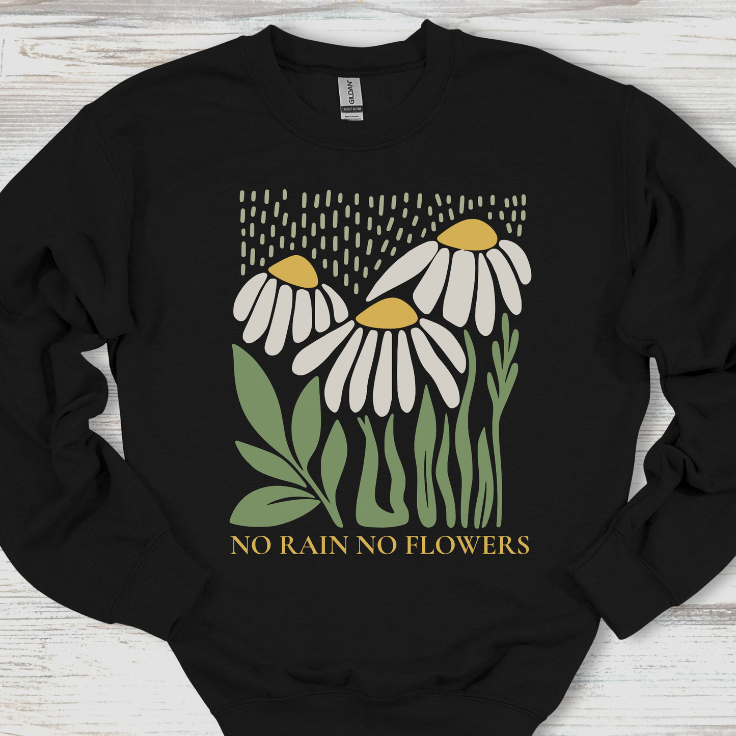 Black sweatshirt with floral design and 'No Rain No Flowers' text on a wooden surface