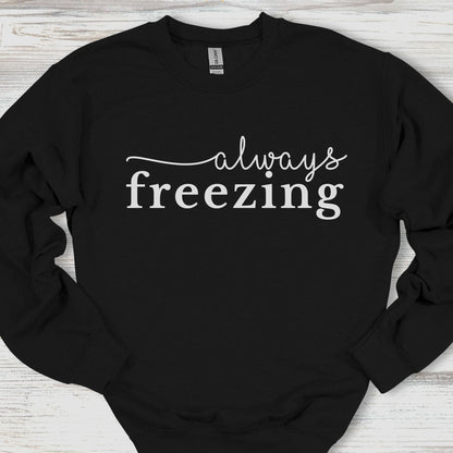 Black sweatshirt with 'always freezing' text on a wooden surface