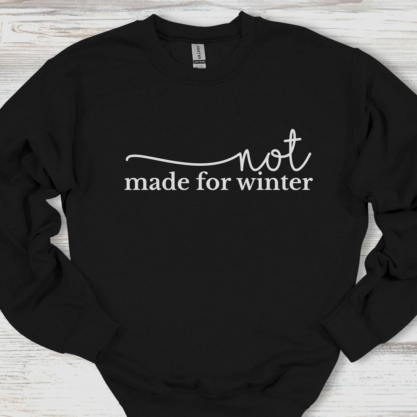 Black sweatshirt with 'not made for winter' text on a wooden surface