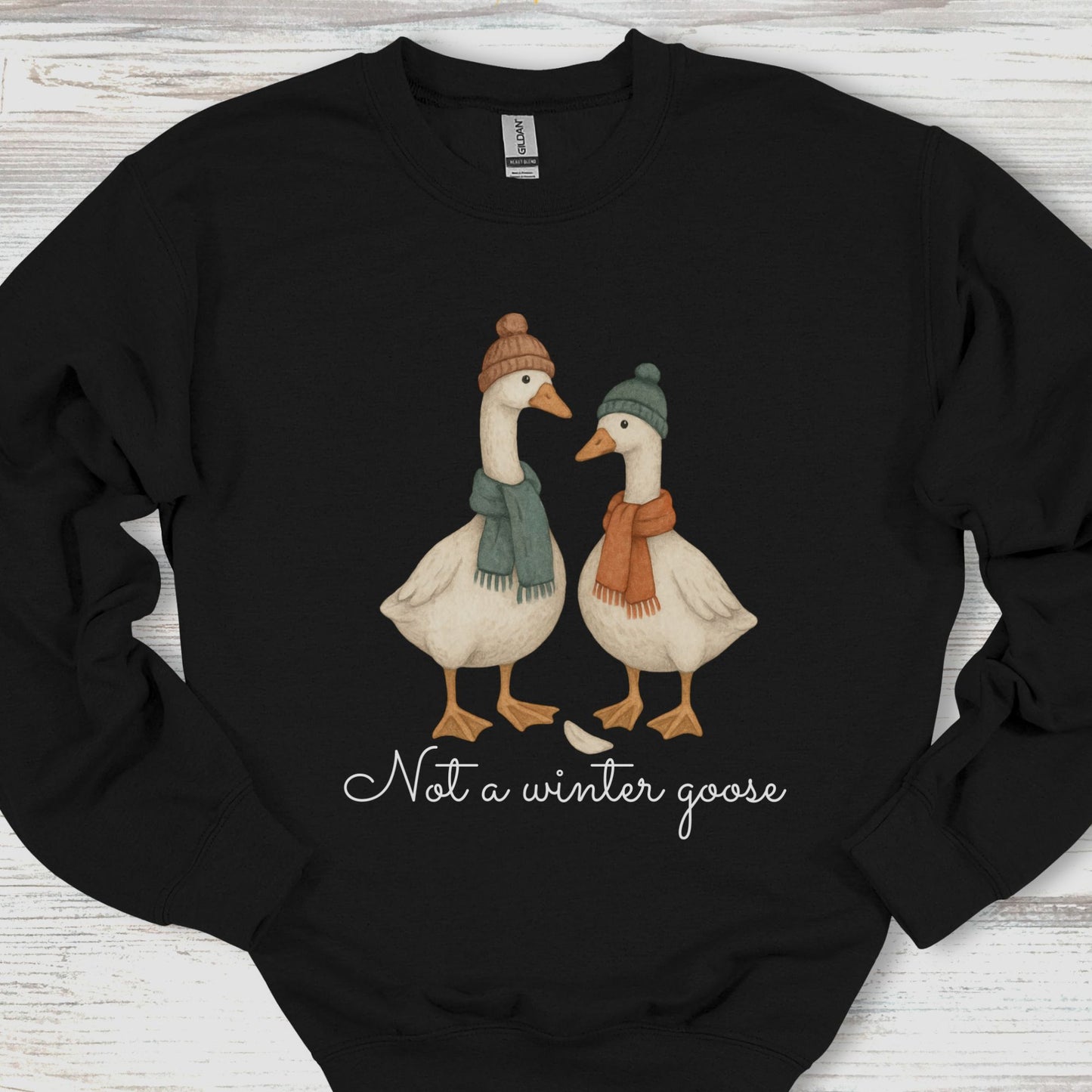 Black sweatshirt with two geese wearing hats and scarves, and text 'Not a winter goose' on a wooden surface.
