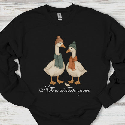 Black sweatshirt with two geese wearing hats and scarves, and text 'Not a winter goose' on a wooden surface.