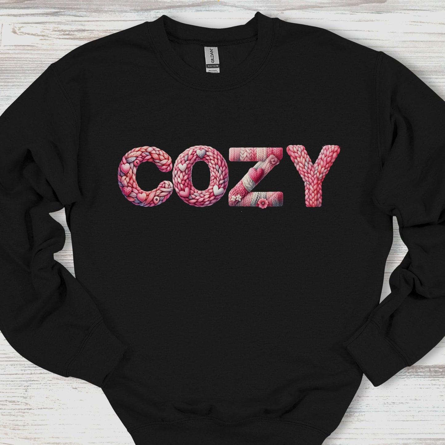 Black sweatshirt with 'COZY' printed in pink on a wooden surface