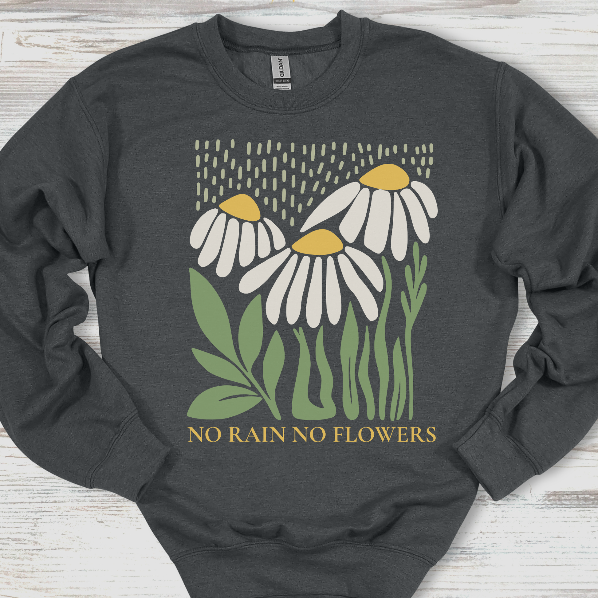 Dark gray sweatshirt with floral design and 'No Rain No Flowers' text on a wooden surface