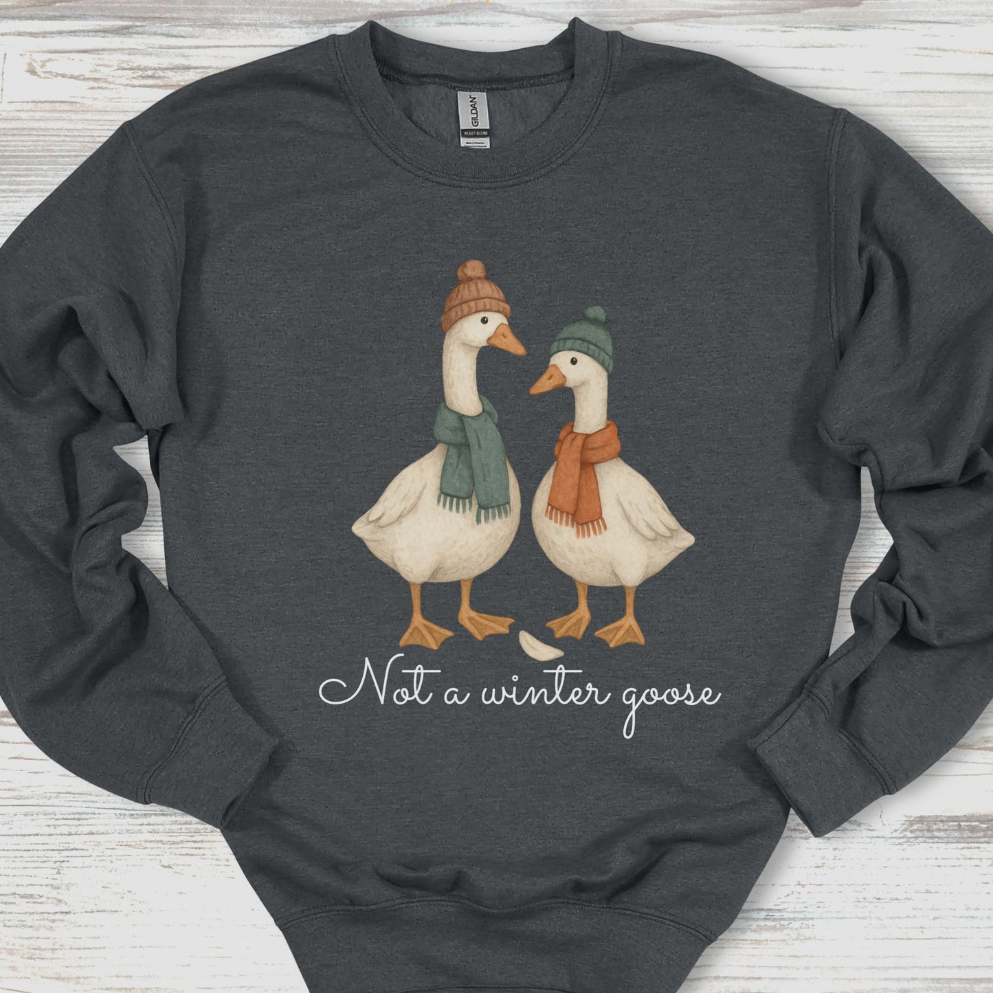 Dark gray sweatshirt with two geese wearing hats and scarves, and text 'Not a winter goose' on a wooden surface.