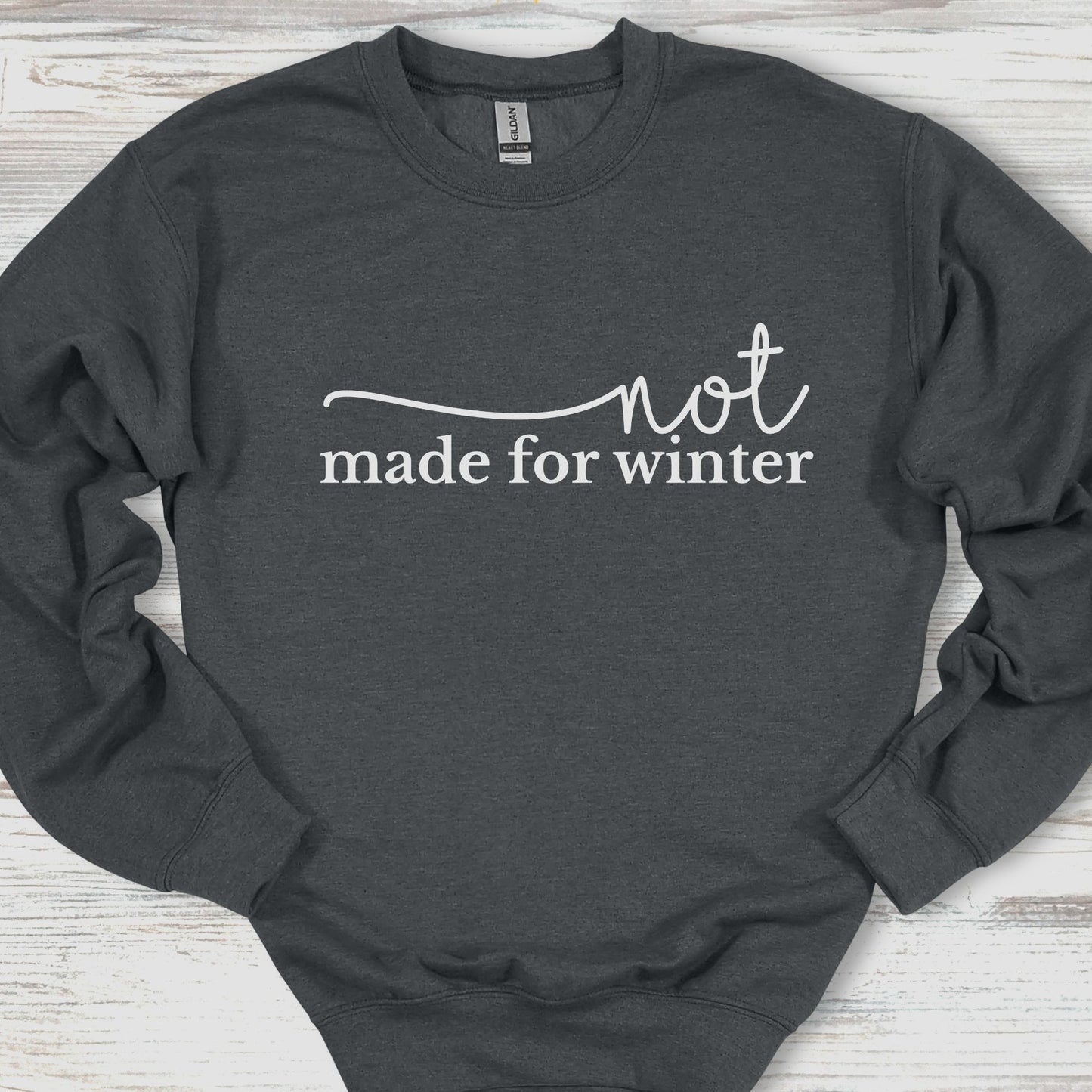 Dark gray sweatshirt with 'not made for winter' text on a wooden surface