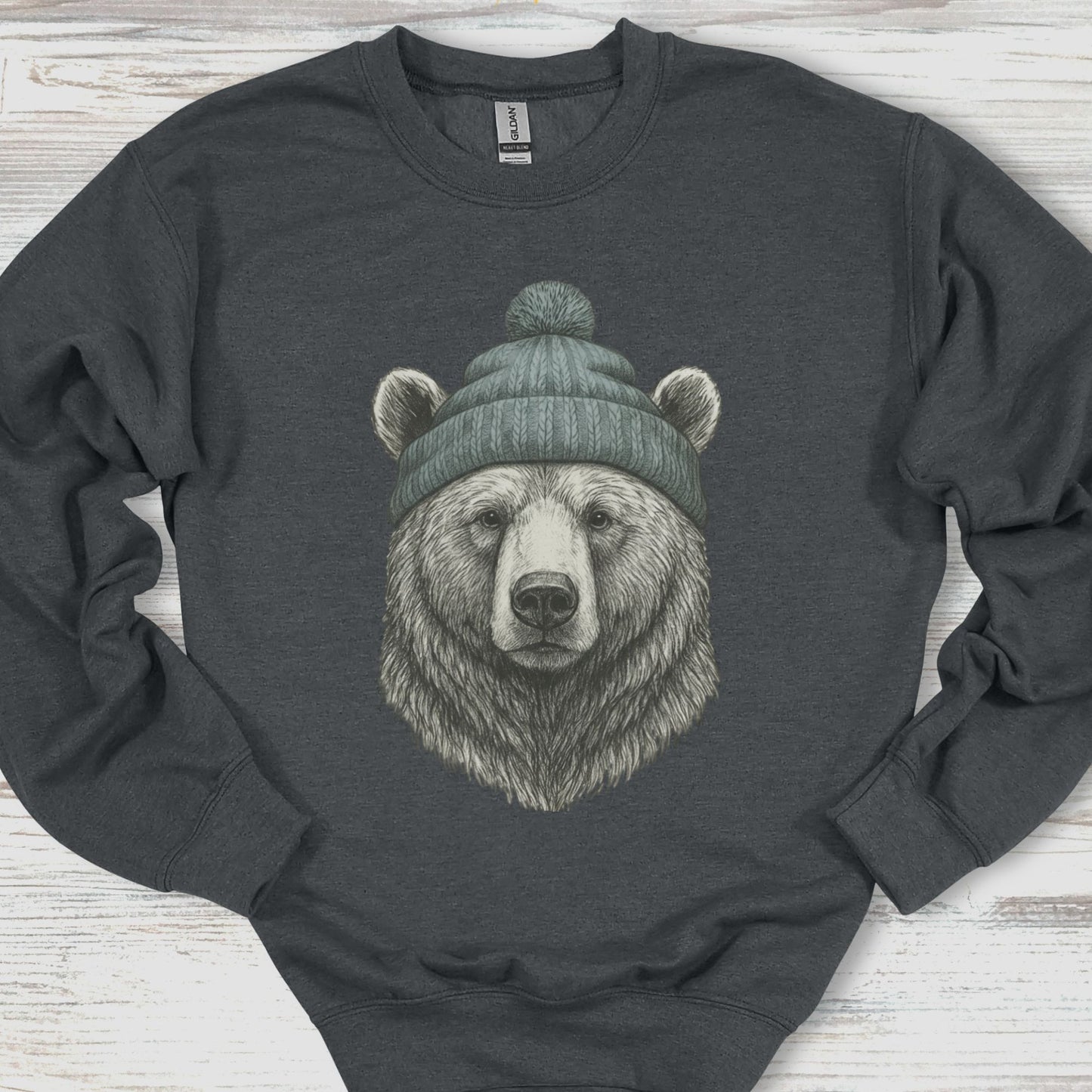 Dark gray sweatshirt with a bear wearing a green beanie on a wooden surface