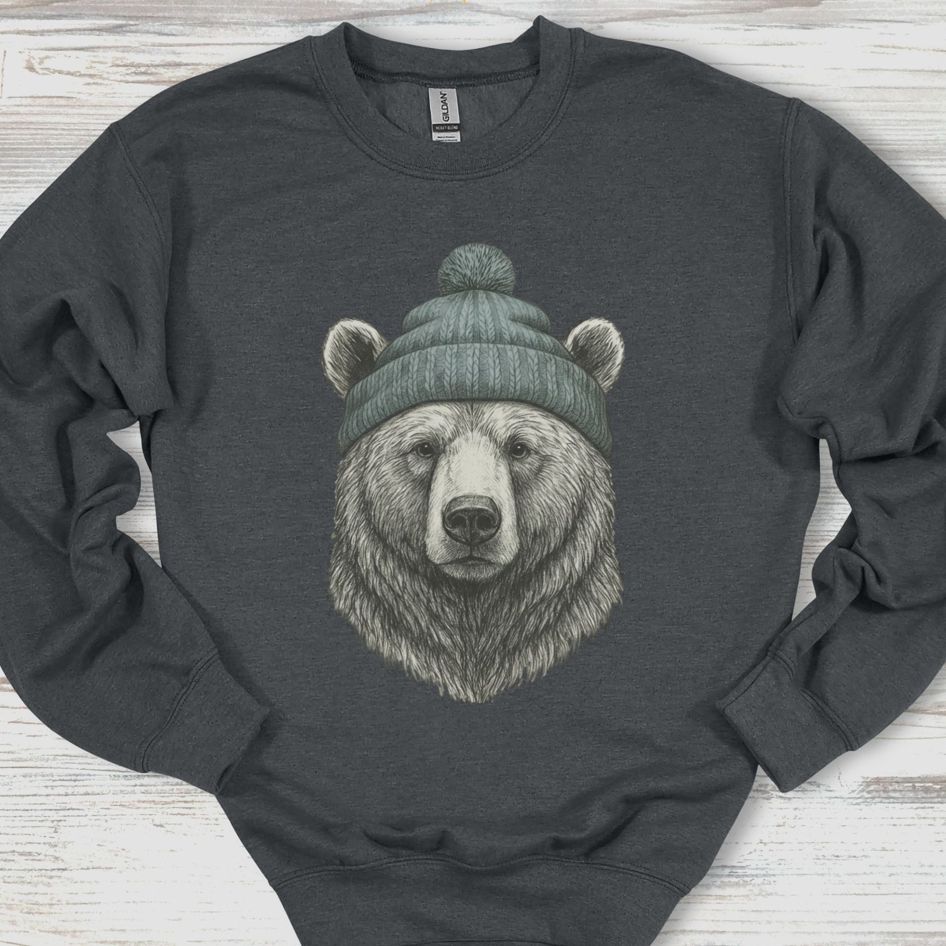 Dark gray sweatshirt with a bear wearing a green beanie on a wooden surface