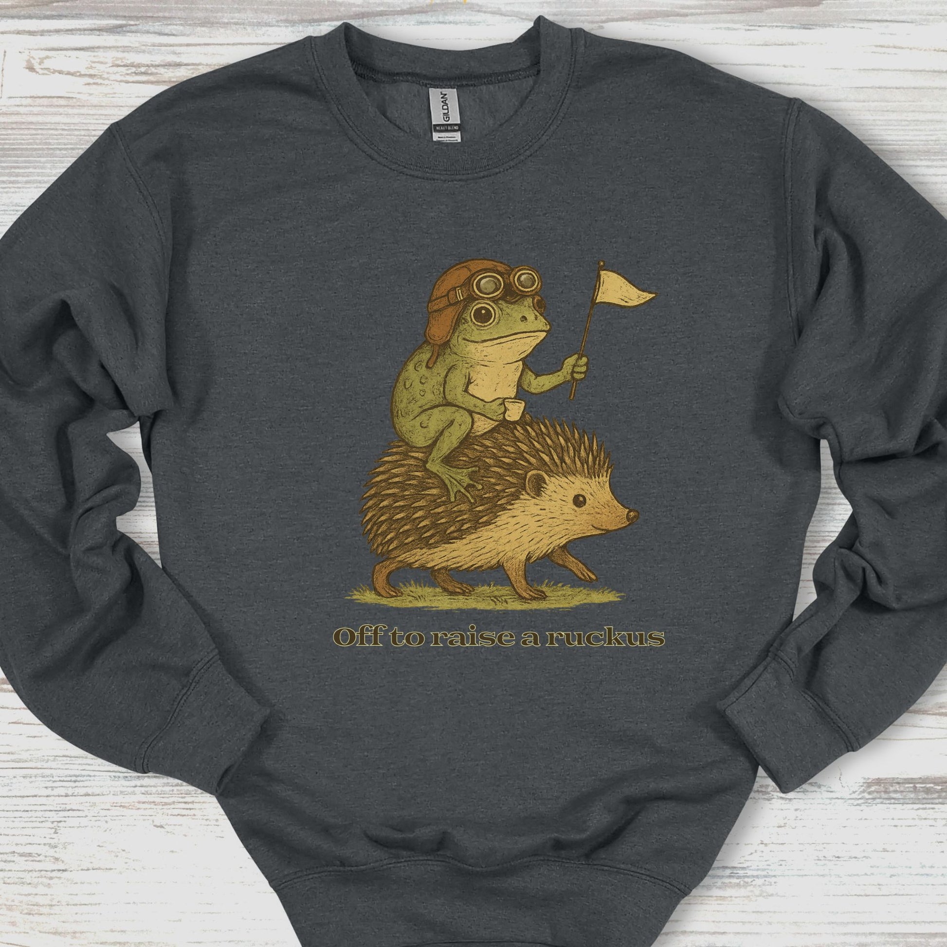 Dark gray sweatshirt with a graphic of a frog and hedgehog riding together, holding a flag, on a wooden surface.
