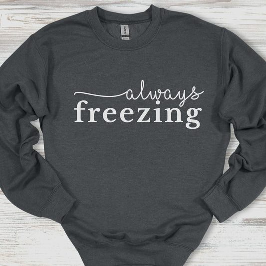 Dark gray sweatshirt with 'always freezing' text on a wooden surface