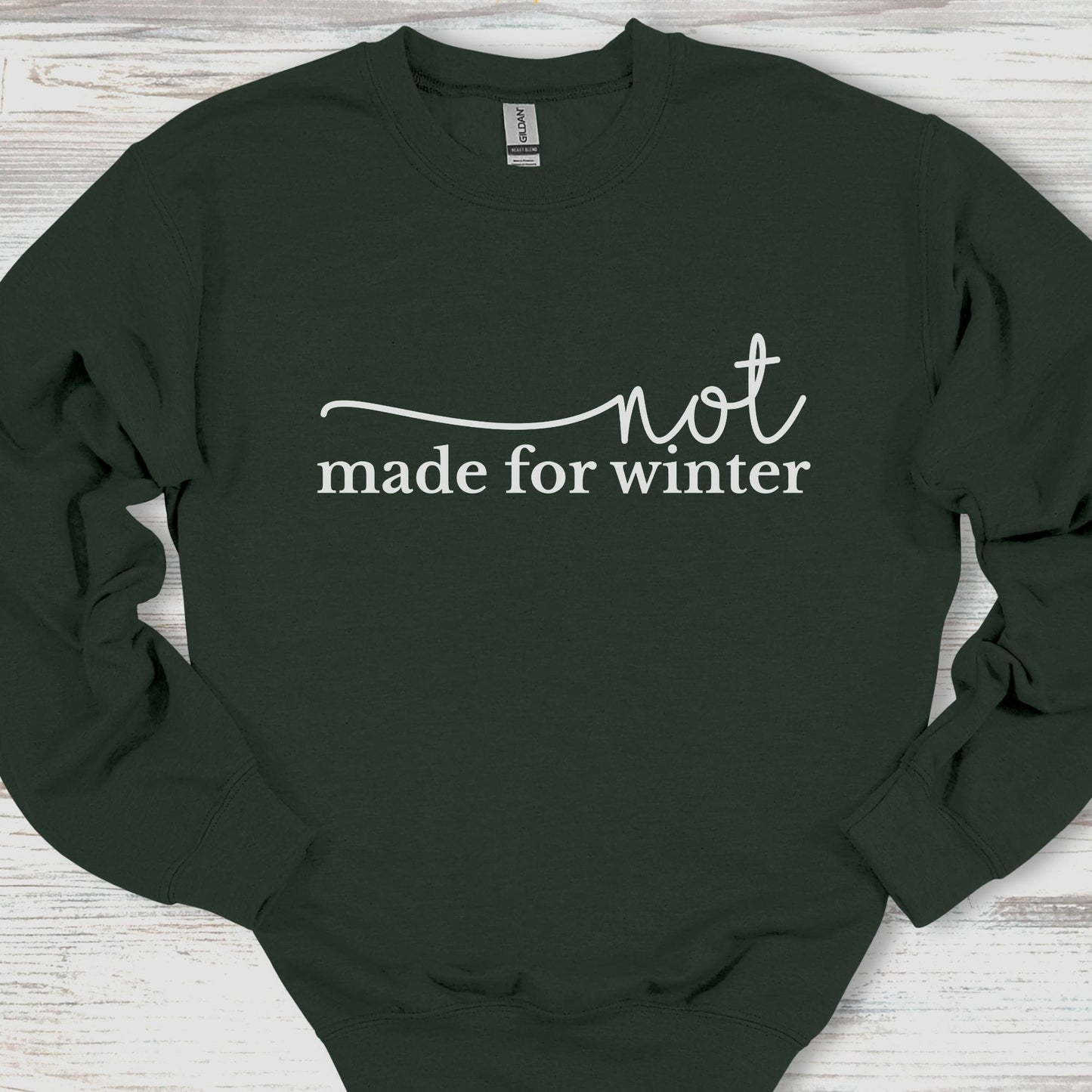 Black sweatshirt with 'not made for winter' text on a wooden surface
