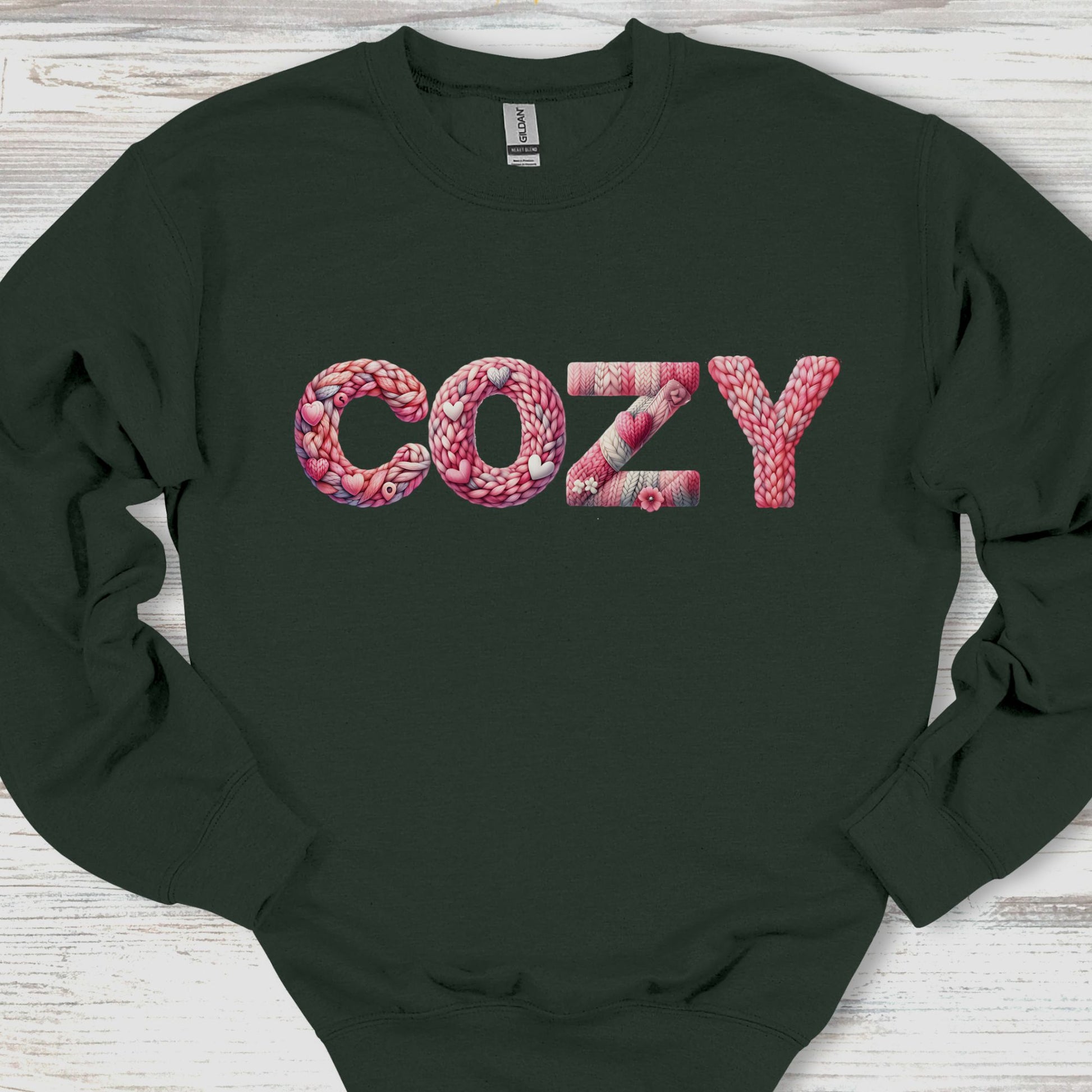 Black sweatshirt with 'COZY' text in pink yarn on a wooden surface
