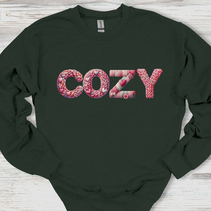 Black sweatshirt with 'COZY' text in pink yarn on a wooden surface