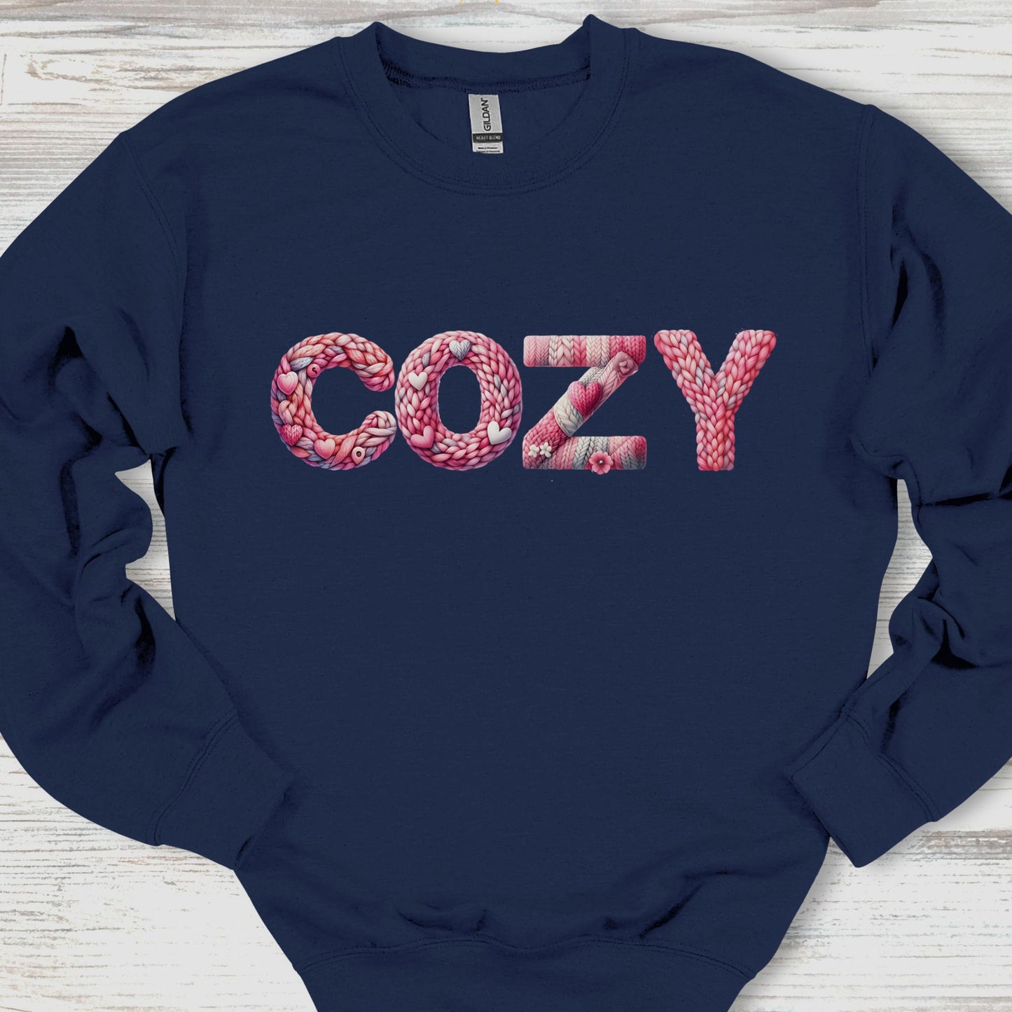 Navy blue sweatshirt with 'COZY' in pink text on a wooden surface