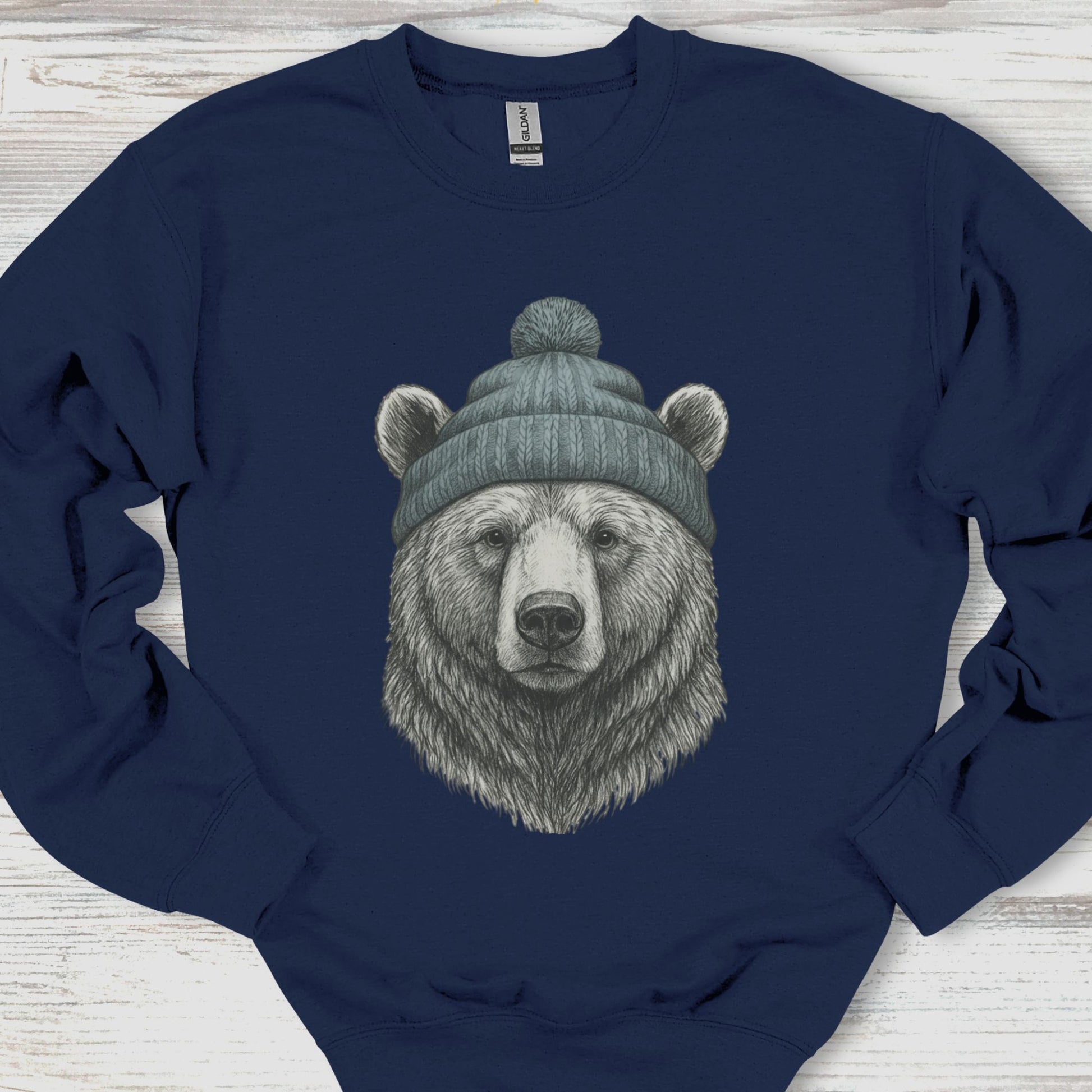 Navy blue sweatshirt with a bear wearing a beanie on a wooden surface