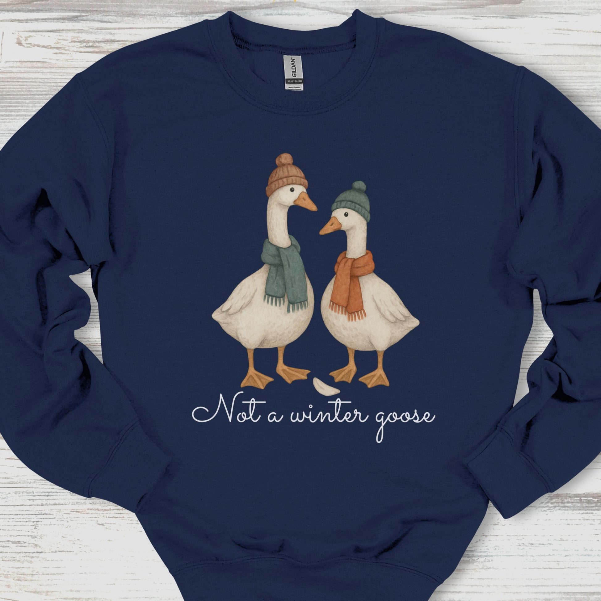 Navy blue sweatshirt with two illustrated geese wearing hats and scarves, and text 'Not a winter goose' on a wooden surface.