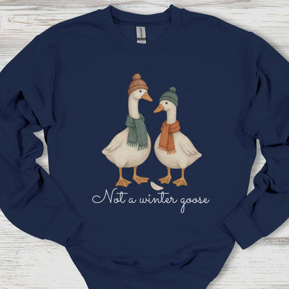 Navy blue sweatshirt with two illustrated geese wearing hats and scarves, and text 'Not a winter goose' on a wooden surface.