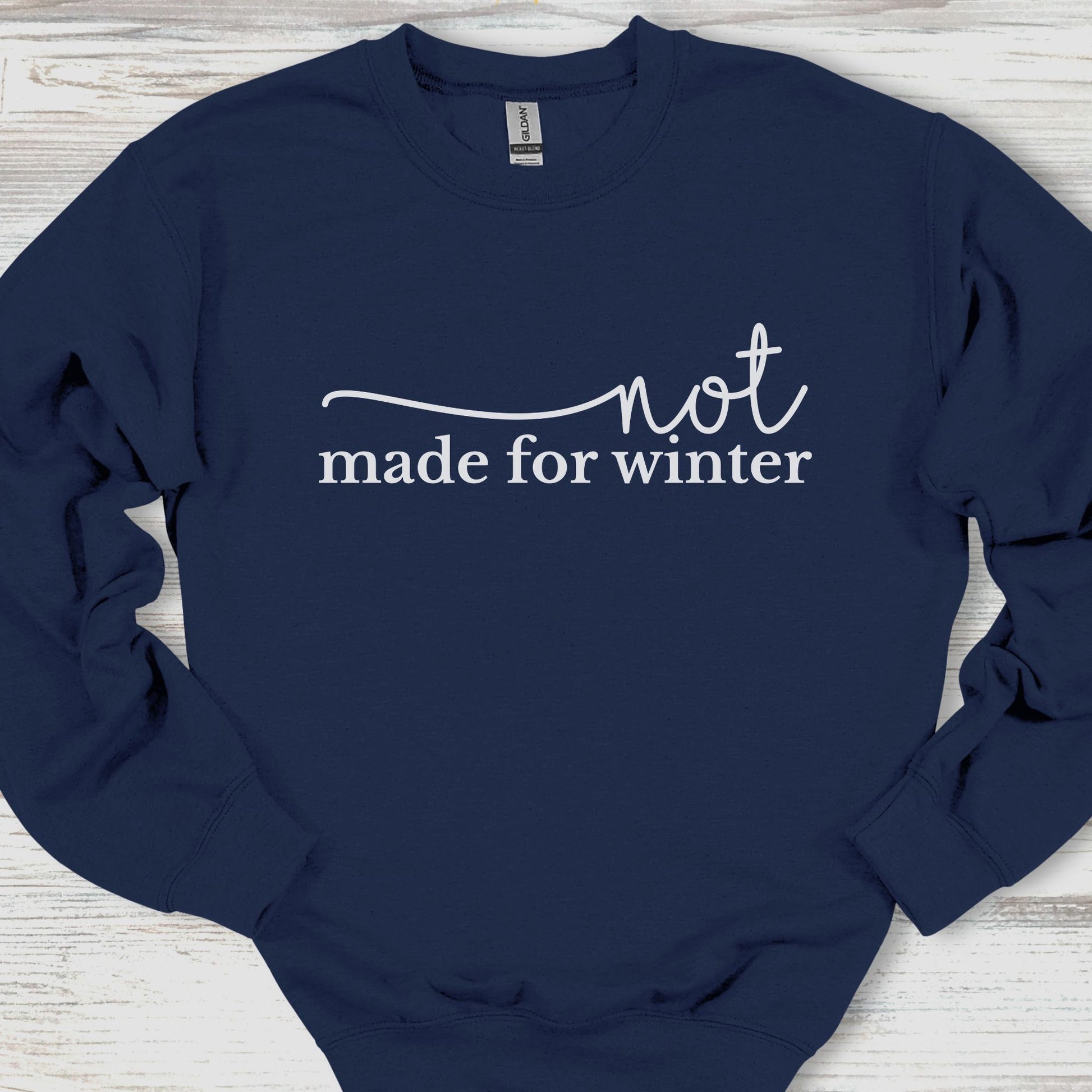 Navy blue sweatshirt with 'not made for winter' text on a wooden surface