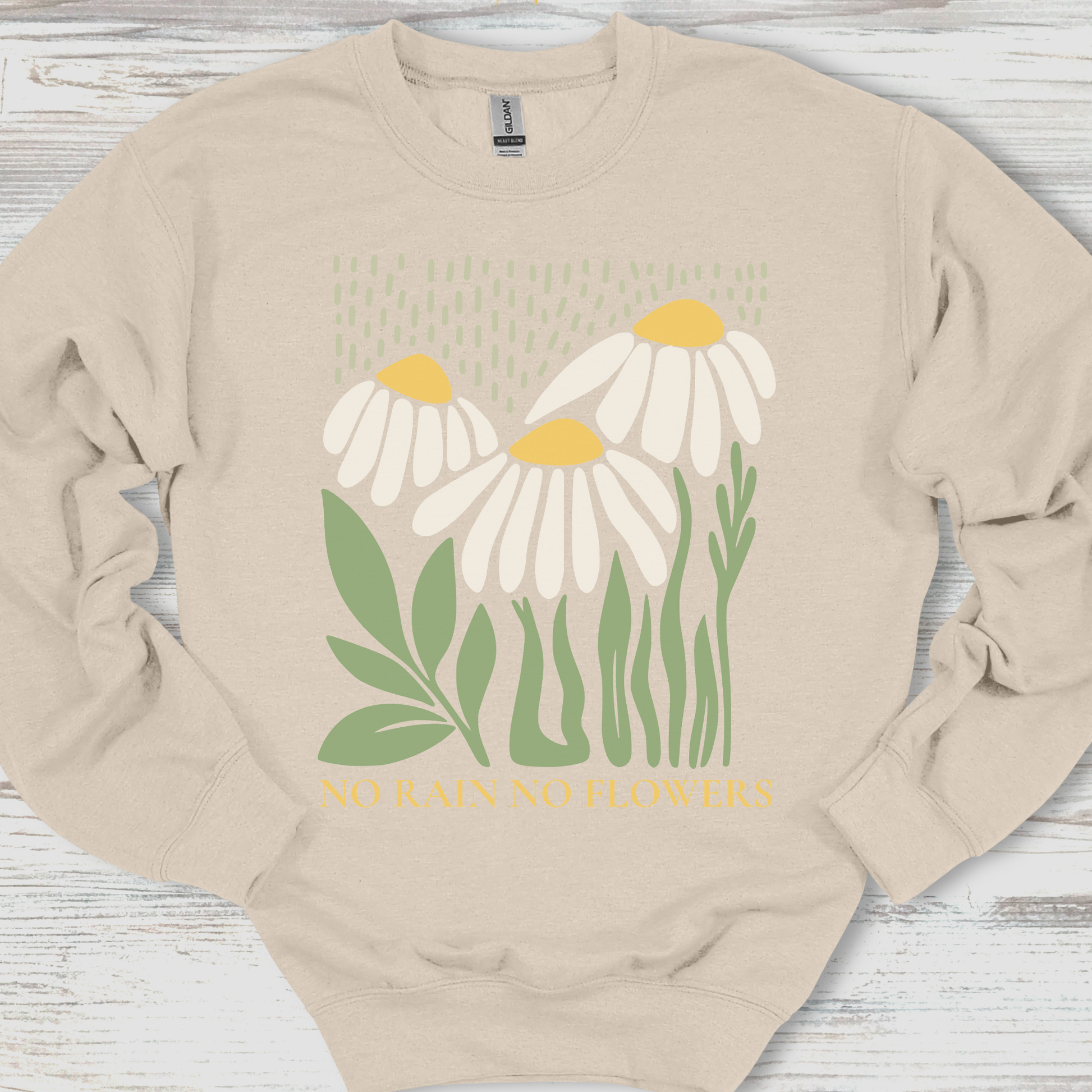 Beige sweatshirt with daisy flower design and text on a wooden surface