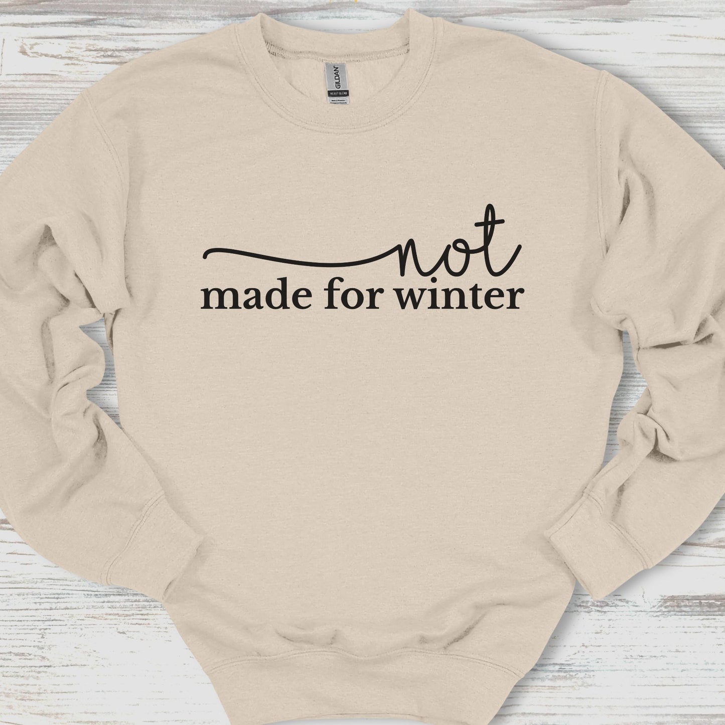 Beige sweatshirt with 'not made for winter' text on a wooden surface
