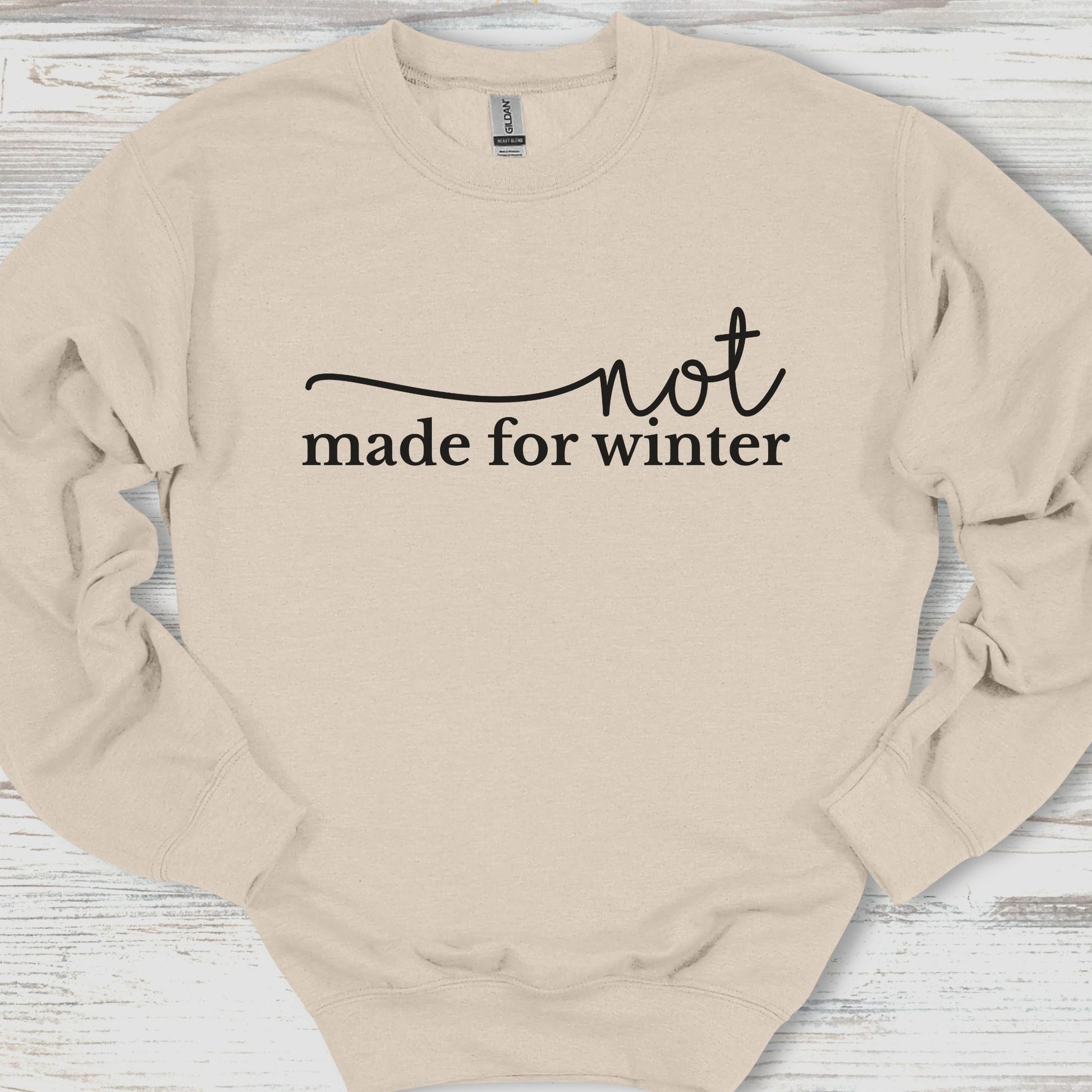 Beige sweatshirt with 'not made for winter' text on a wooden surface