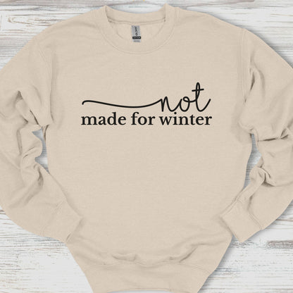 Beige sweatshirt with 'not made for winter' text on a wooden surface