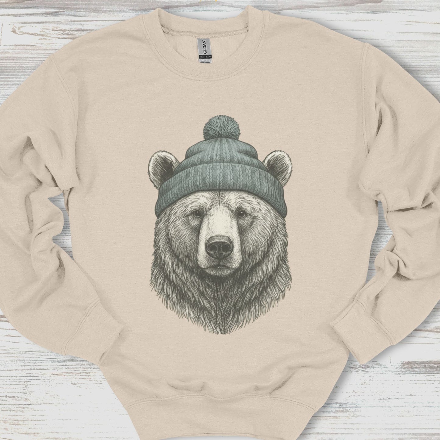 Beige sweatshirt with a bear wearing a beanie design on a wooden surface