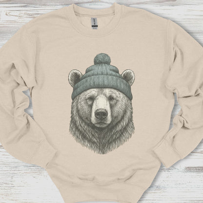 Beige sweatshirt with a bear wearing a beanie design on a wooden surface