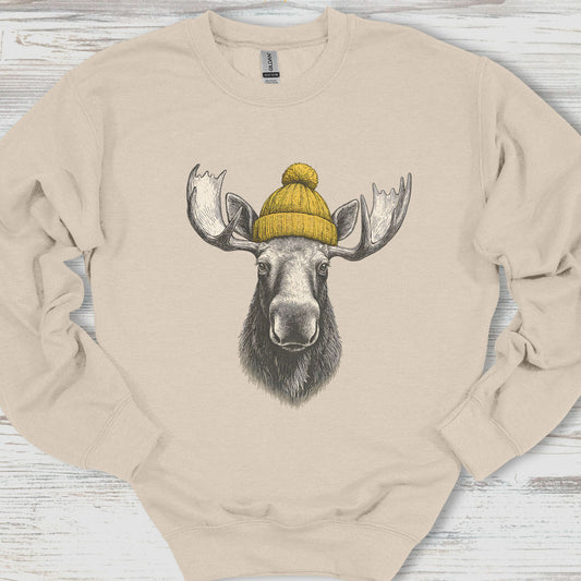 Beige sweatshirt with a moose wearing a yellow beanie on a wooden surface