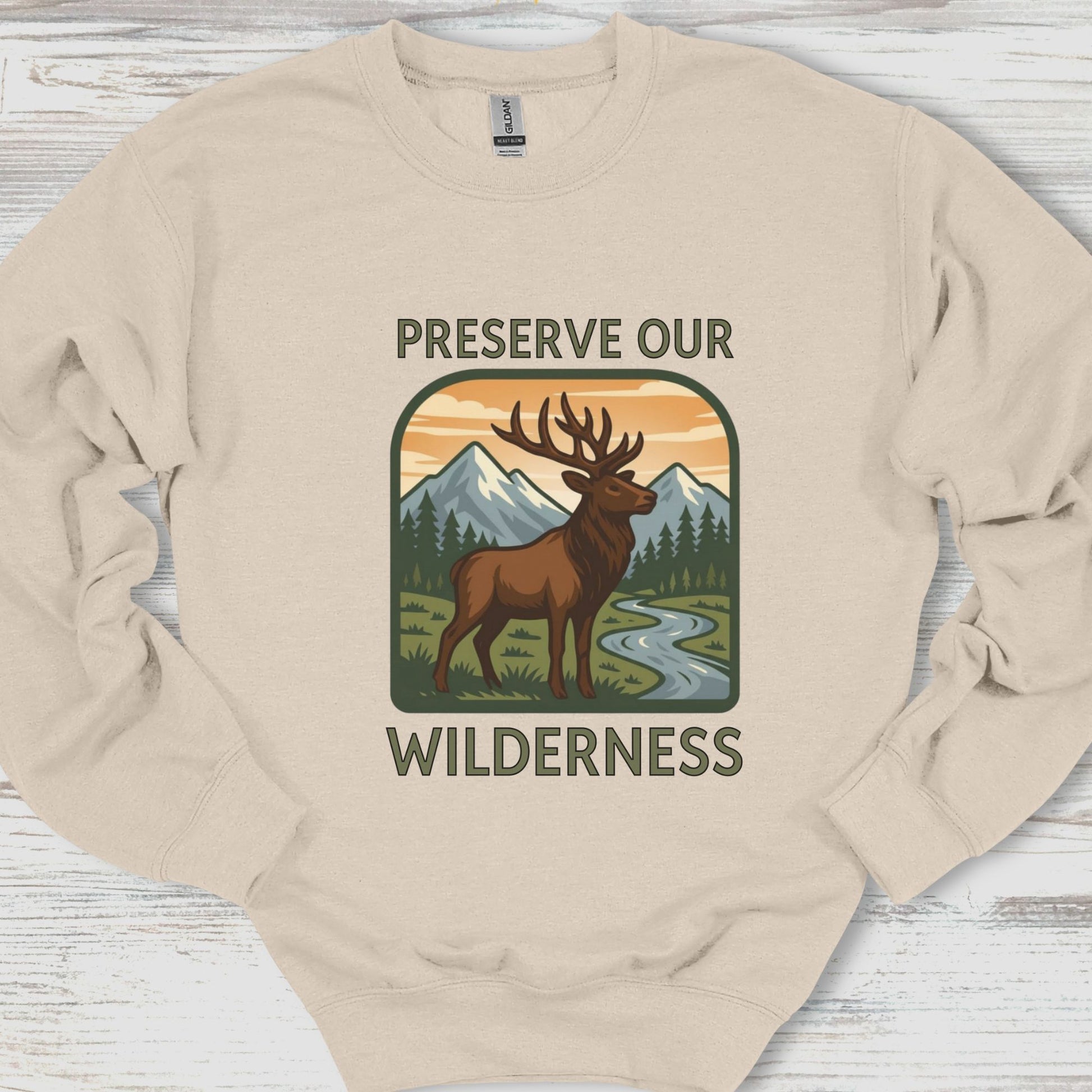 Beige sweatshirt with a graphic of a deer and mountains and text 'Preserve Our Wilderness' on a wooden surface.