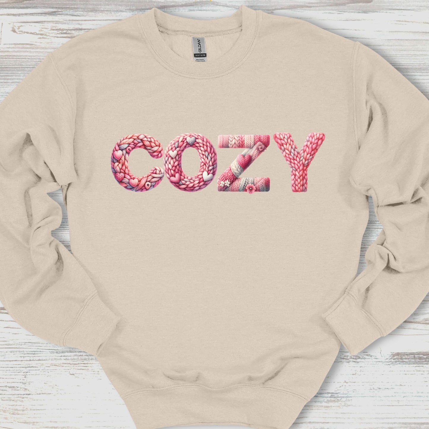 Beige sweatshirt with 'COZY' printed in pink letters on a wooden surface