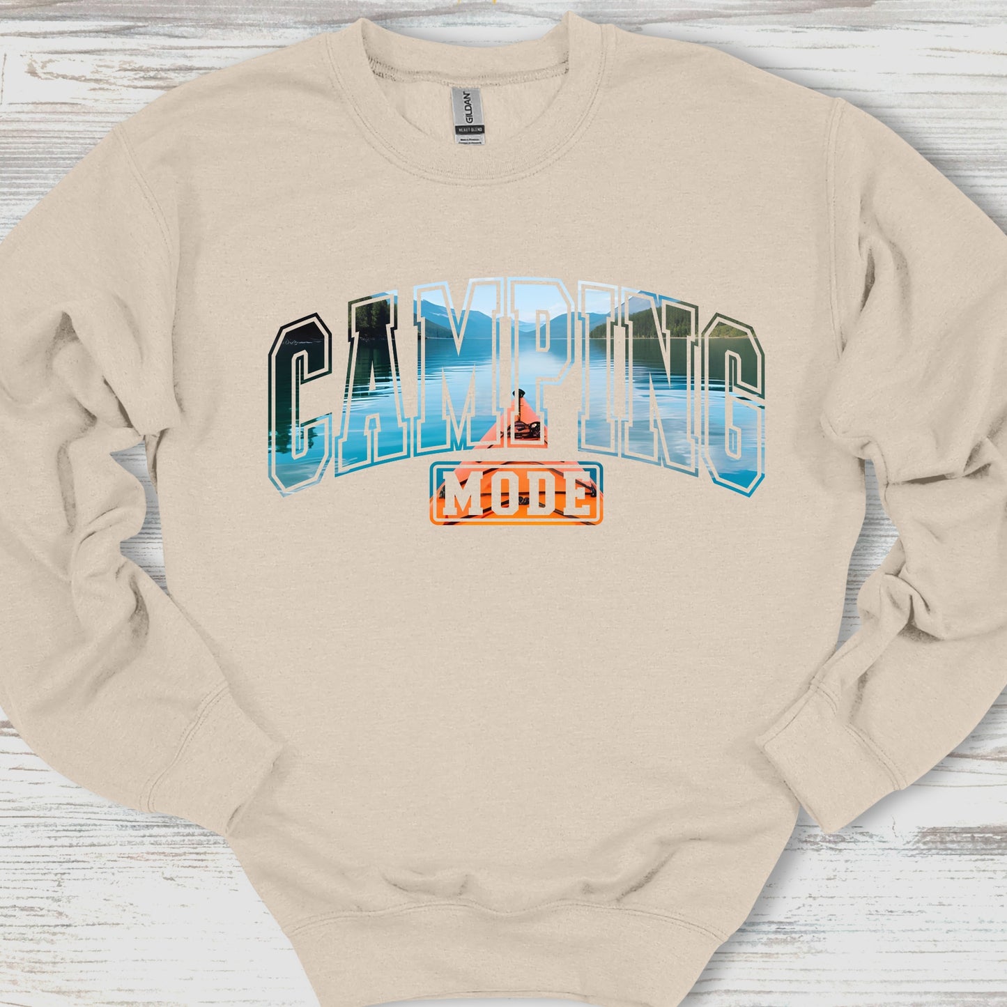 Beige sweatshirt with 'Camping Mode' graphic on a wooden surface