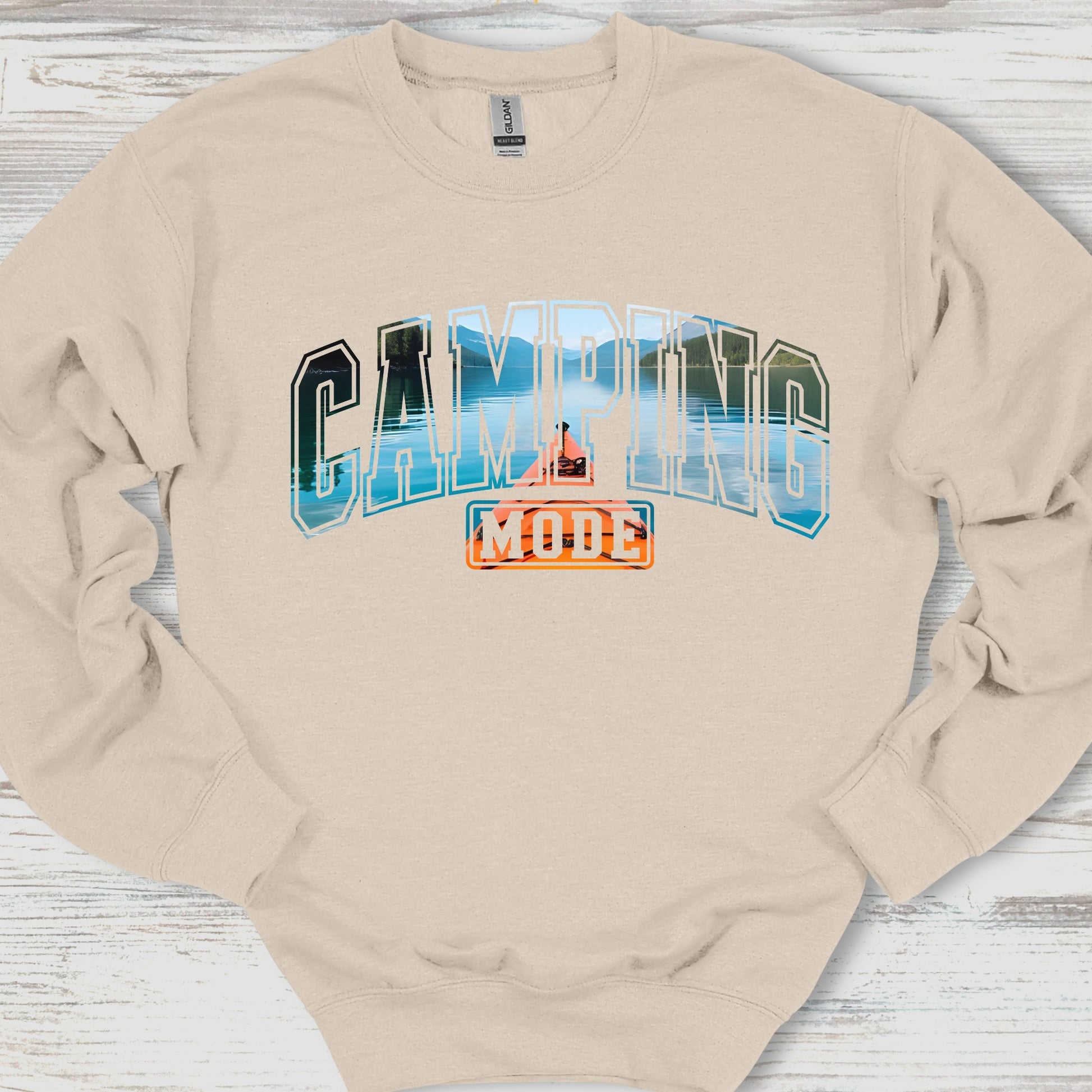 Beige sweatshirt with 'Camping Mode' graphic on a wooden surface