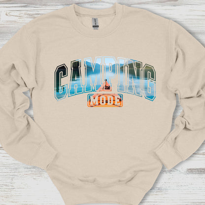 Beige sweatshirt with 'Camping Mode' graphic on a wooden surface