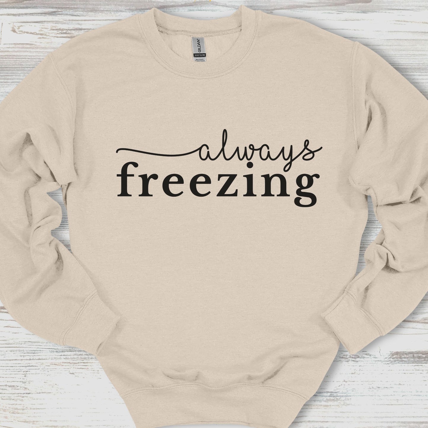 Beige sweatshirt with 'always freezing' text on a wooden surface