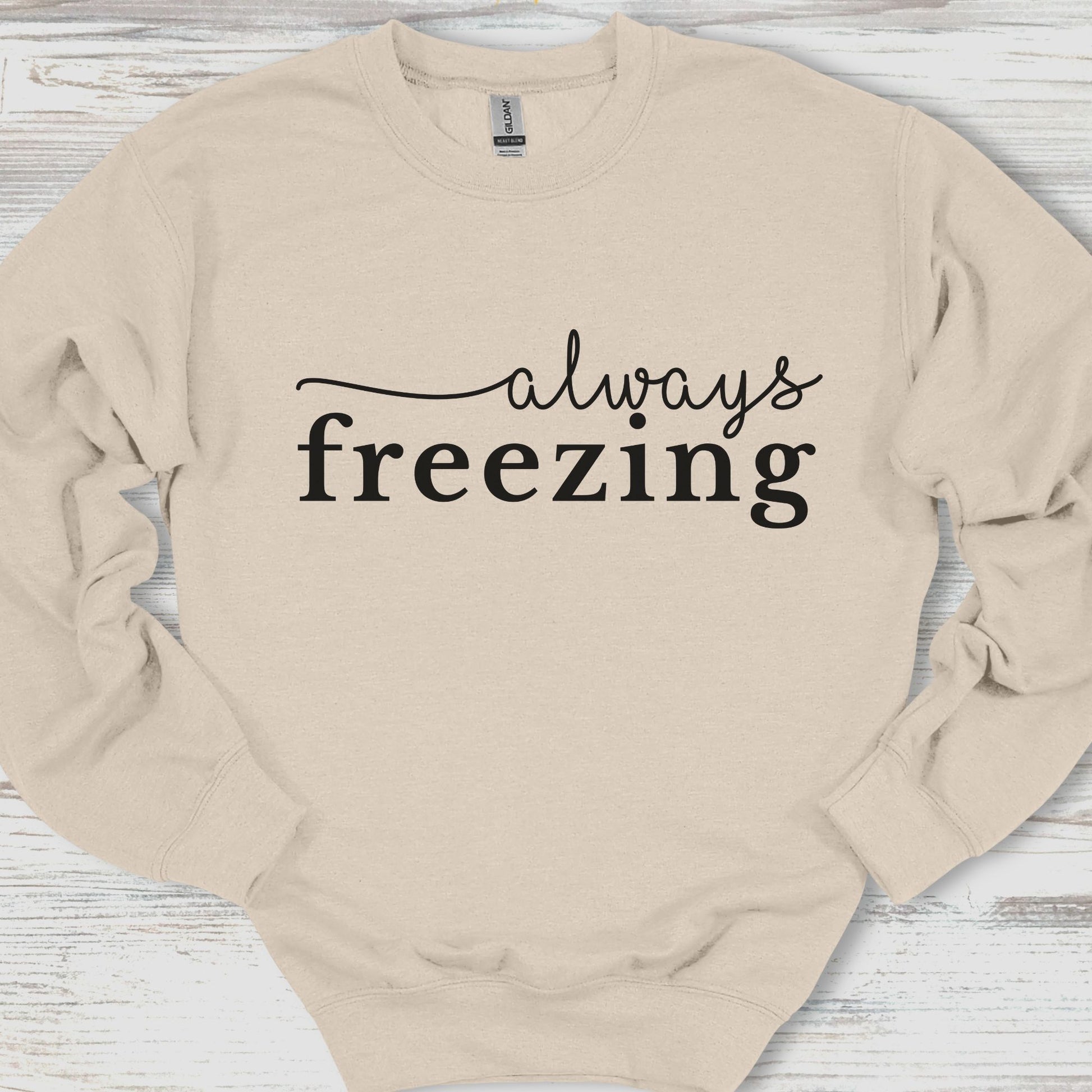 Beige sweatshirt with 'always freezing' text on a wooden surface