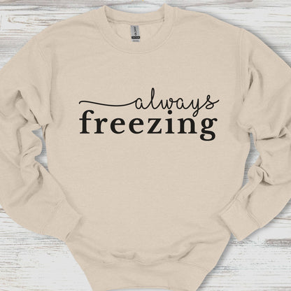 Beige sweatshirt with 'always freezing' text on a wooden surface