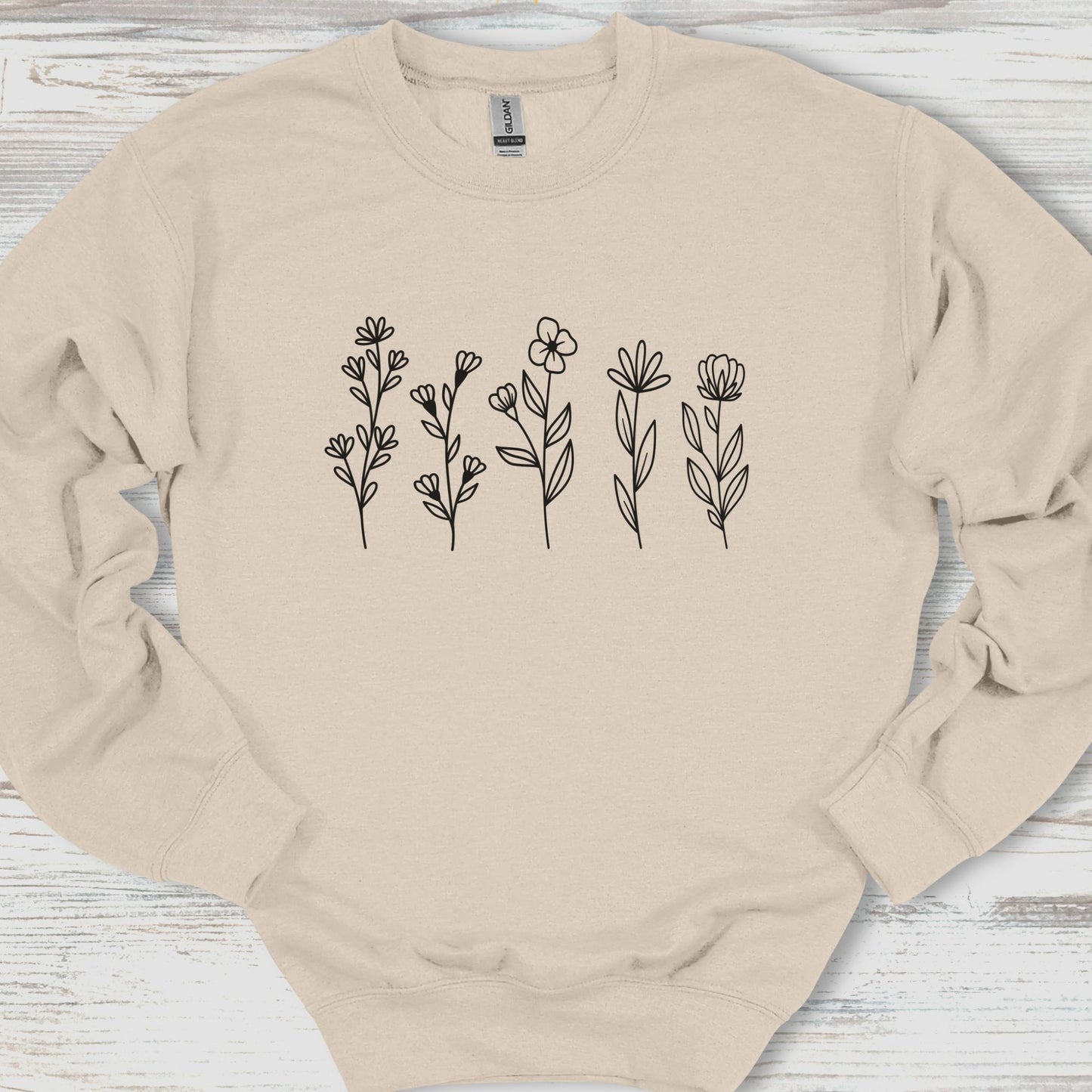 Beige sweatshirt with floral designs on a wooden surface